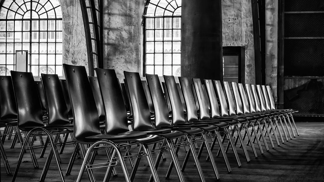 Une longue rangée de chaises alignées dans une salle, en noir et blanc